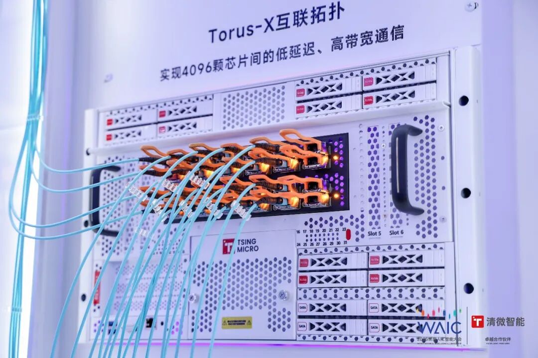 图片展示了TsingMicro在WAIC 2026上展示的4K supernode概念中的Torus-X互联拓扑。背景板上标注“Torus-X互联拓扑,实现4096颗芯片间的低延迟、高带宽通信”。画面中,4096颗TX81处理器通过网格状网络组织,处理器间有大量蓝色光纤连接,部分光纤上有黄色指示灯。该图片与文档中TsingMicro在WAIC 2026上展示4K supernode概念的内容相关,直观呈现了其架构。