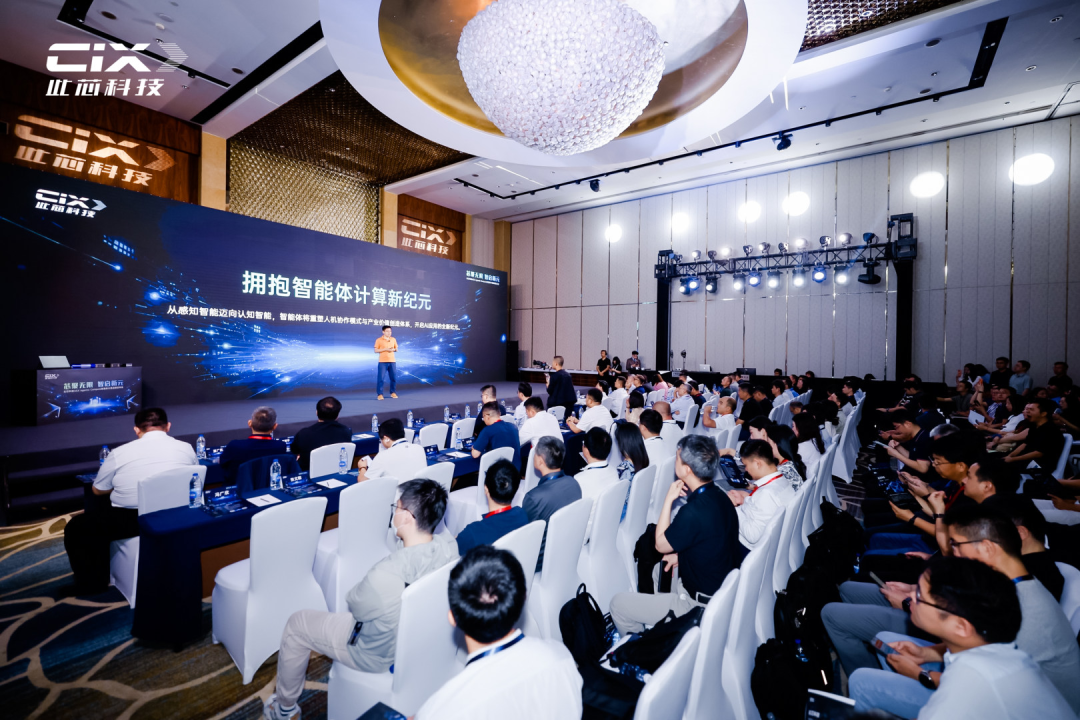 图片展示的是中国芯片公司CIX在2026年世界人工智能大会(WAIC)上发布AGX Agentic Compute策略及AGX Station系统的场景。画面中,一位身穿浅色上衣的演讲者站在舞台左侧,身后大屏幕上显示着“拥抱智能体计算新纪元”的文字。舞台上方悬挂着大型装饰灯,两侧有CIX的标志。台下观众席上坐满了人,部分人手持笔记本电脑。此图与上文介绍CIX在WAIC 2026期间发布AGX Station等内容相呼应。