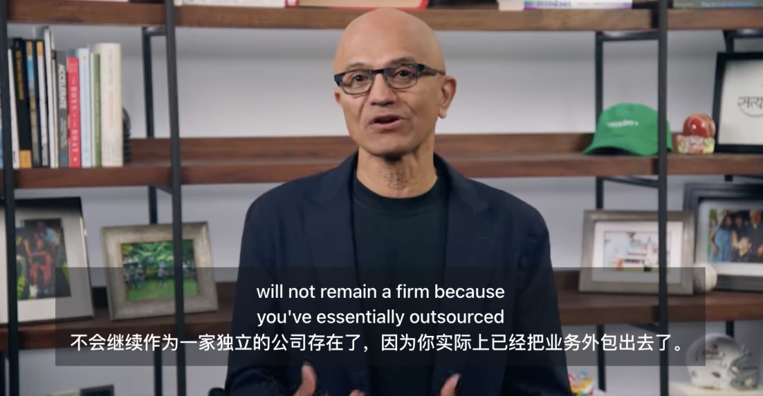 Imagem mostra o CEO da Microsoft, Satya Nadella, vestindo terno preto, com uma estante de livros ao fundo contendo livros, chapéus e outros itens. Abaixo da imagem, há legendas bilíngues em chinês e inglês. A legenda em chinês diz "não continuará existindo como uma empresa independente, porque você terceirizou essencialmente o negócio". A legenda em inglês diz "will not remain a firm because you've essentially outsourced". A imagem está intimamente relacionada ao contexto, que menciona o aviso de Nadella sobre os riscos das empresas em plataformas de IA, enfatizando que as empresas devem manter o controle sobre dados, prompts, metadados, etc. O conteúdo da legenda ecoa esse ponto de vista, elaborando ainda mais as consequências da perda de controle.