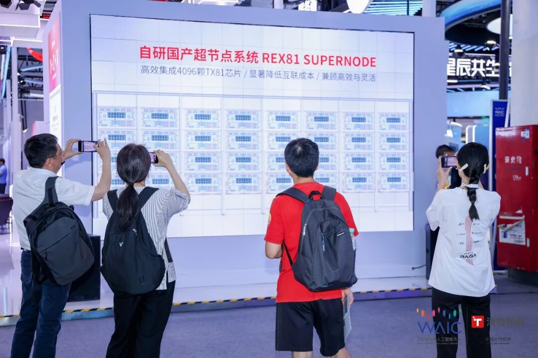 图片展示了TsingMicro在WAIC 2026展会上的展位。展位上方大屏幕显示“自研国产超节点系统REX81 SUPERNODE”及相关信息,下方是该系统的架构图。展位前有四人正在拍照,其中两人手持手机,一人手持相机,一人手持平板。展位背景为蓝色,左侧有红色的“WAIC”标识。此图片与上下文紧密相关,直观呈现了TsingMicro在本次展会中展示的自研国产超节点系统,体现了其全栈计算策略。