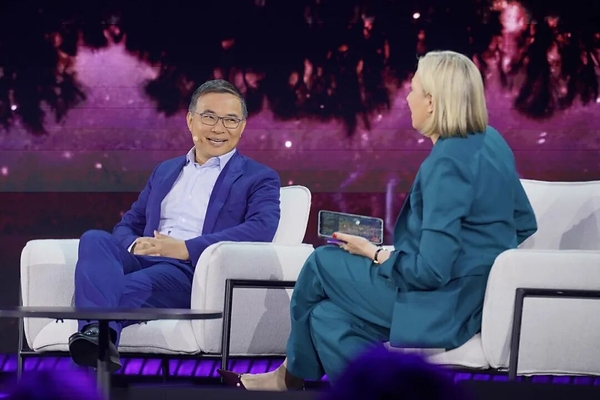 图片显示两位嘉宾在台上交谈。左侧嘉宾身着蓝色西装、白色衬衫,戴着眼镜,坐在白色沙发上;右侧嘉宾身着蓝色西装,手持手机,同样坐在白色沙发上。背景为深色,带有紫色灯光效果和模糊的树纹图案。此图紧接上文介绍AI数据中心电力瓶颈的内容,可能作为相关讨论或采访的视觉呈现,呼应上文内容。