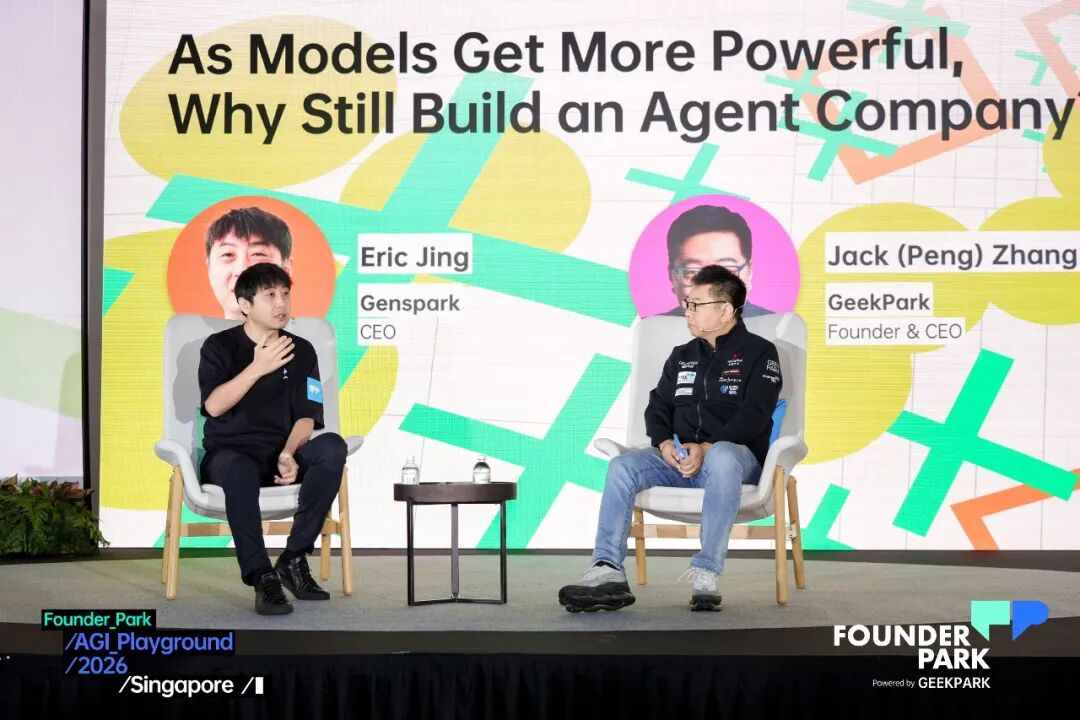 这张图片拍摄于2026年新加坡AGI Playground活动的论坛现场,Genspark CEO Eric Jing与GeekPark创始人兼CEO Jack(Peng)Zhang正在台上进行对话,两人分别坐在白色座椅上,背景大屏显示活动主题“As Models Get More Powerful, Why Still Build an Agent Company”,同时标注出两人的身份与所属机构,舞台上还摆放了小茶几及瓶装饮用水,背景处可见活动主办方相关标识。该图片还原了文档中提及的两人对谈场景,对应文档中关于此次AGI Playground 2026活动的相关内容呈现。