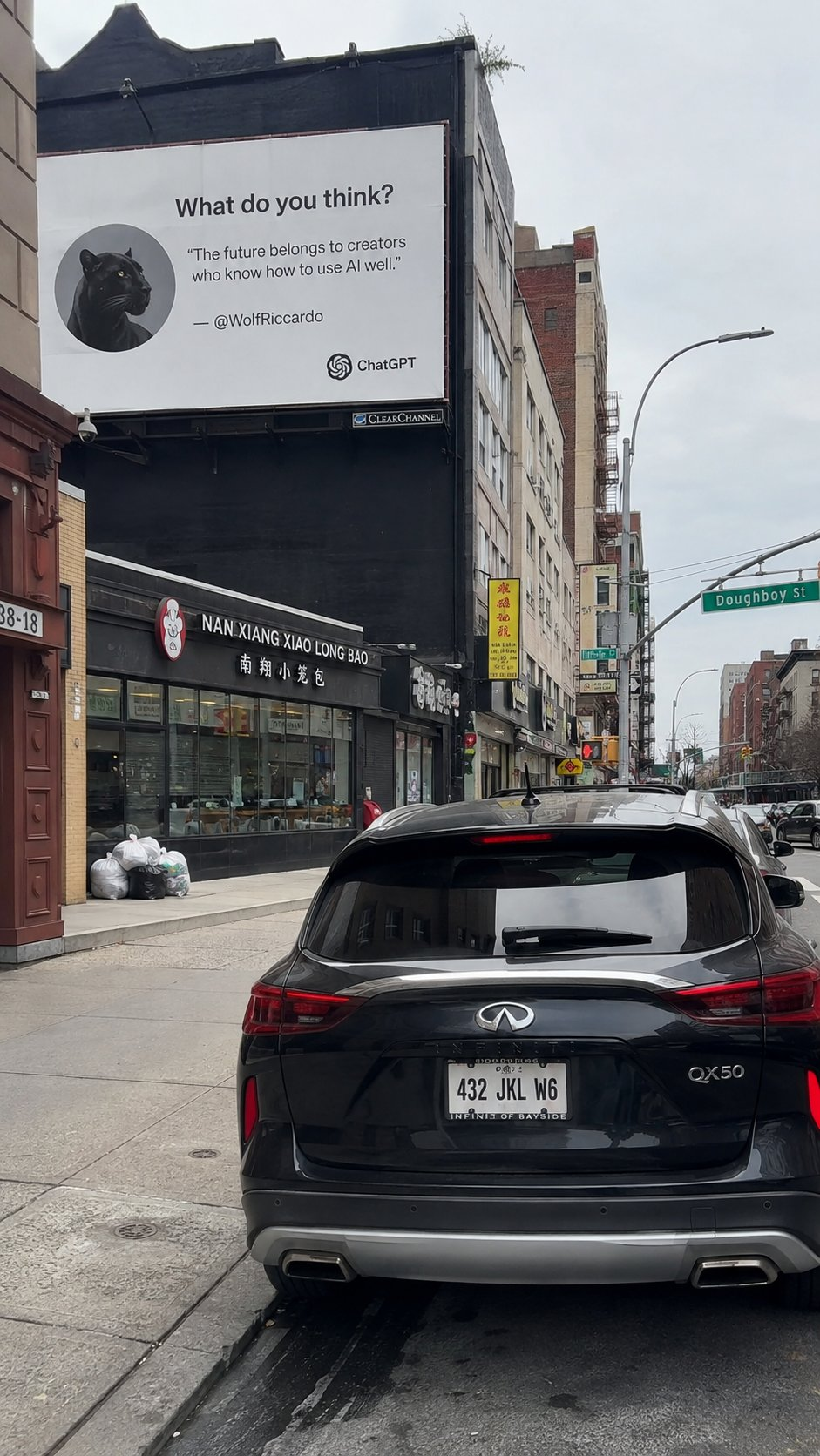 图片展示了城市街边的实景,画面近处是一辆黑色英菲尼迪QX50汽车的车尾,车牌号为432 JKL WG。街边建筑上有一块大型广告牌,带有黑豹头像图案,上面印有英文文字“What do you think?”,以及“The future belongs to creators who know how to use AI well.”,还标注了创作者@WolfRiccardo和ChatGPT的标识。广告牌下方是一家名为“NAN XIANG XIAO LONG BAO”的小笼包店铺,街道旁还有路牌、其他车辆与建筑,呈现出充满生活感的都市街景。